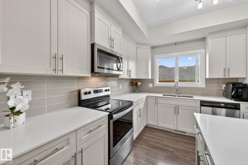 Kitchen featuring white shaker-style cabinetry, stainless steel appliances, white countertops, and a neutral tile backsplash - 165 Robinson Drive, Leduc, AB 