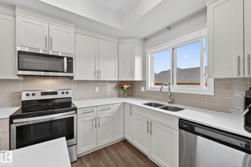 Modern kitchen featuring white cabinetry, light-toned linear tile backsplash, and wood-finish flooring - 165 Robinson Drive, Leduc, AB 