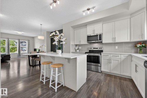 Modern kitchen featuring white cabinetry, stainless steel appliances, a light-toned backsplash, and a central island with an extended countertop - 165 Robinson Drive, Leduc, AB 