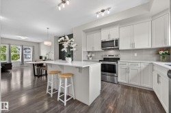 Modern kitchen featuring white cabinetry, stainless steel appliances, a light-toned backsplash, and a central island with an extended countertop - 