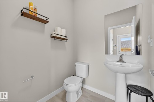 Bathroom featuring a pedestal sink with chrome faucet, a white toilet, and light-toned tile flooring - 165 Robinson Drive, Leduc, AB 