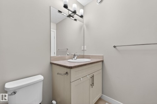 Bathroom featuring a neutral palette, a light wood-finish vanity with dual cabinet doors, a beige countertop, an undermount sink, and a large wall-mounted mirror with overhead lighting - 165 Robinson Drive, Leduc, AB 