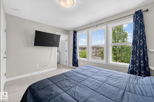 Carpeted bedroom featuring three multi-pane windows, a ceiling-mounted light fixture, white trim, and a wall-mounted television - 165 Robinson Drive, Leduc, AB 