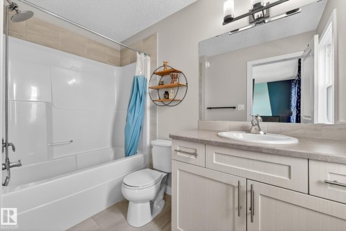 Bathroom featuring a white bathtub with an integrated shower, a vanity with a light-toned countertop, an undermount sink with a chrome faucet, light wood-finish cabinetry, and a large wall-mounted mirror - 165 Robinson Drive, Leduc, AB 