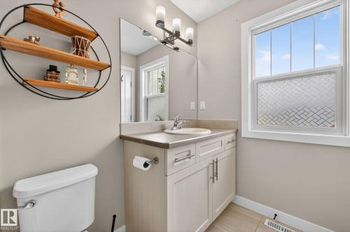Bathroom featuring a single vanity with stone-finish countertop, white cabinetry with brushed nickel hardware, and a framed mirror - 165 Robinson Drive, Leduc, AB 