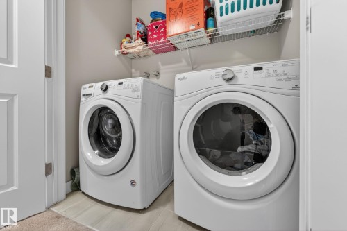 Dedicated laundry space featuring a front-loading washer and dryer, light-toned wall paint, and overhead wire shelving - 165 Robinson Drive, Leduc, AB 