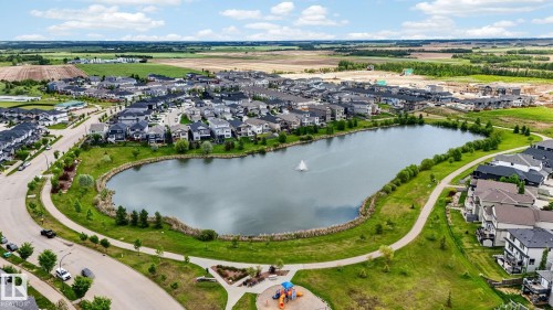 Master-planned community featuring a central lake with a fountain, surrounding green spaces, paved walking paths, and a visible playground structure - 165 Robinson Drive, Leduc, AB 