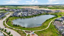 Master-planned community featuring a central lake with a fountain, surrounding green spaces, paved walking paths, and a visible playground structure - 