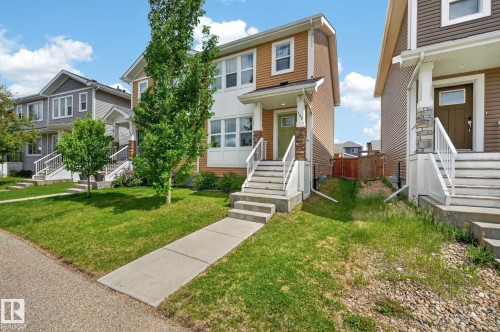 Contemporary two-story residence featuring a front porch with white railings, stone pillar accents, and a light green entry door - 165 Robinson Drive, Leduc, AB 