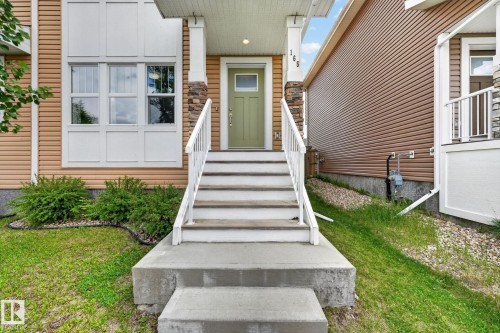 Exterior featuring light brown siding, a light green entry door, concrete steps with white railings, and decorative stone column accents - 165 Robinson Drive, Leduc, AB 