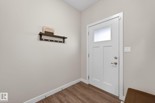 White paneled entry door with frosted glass insert, satin nickel hardware, wood-finish flooring, and light neutral wall paint - 165 Robinson Drive, Leduc, AB 