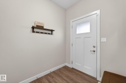 White paneled entry door with frosted glass insert, satin nickel hardware, wood-finish flooring, and light neutral wall paint - 
