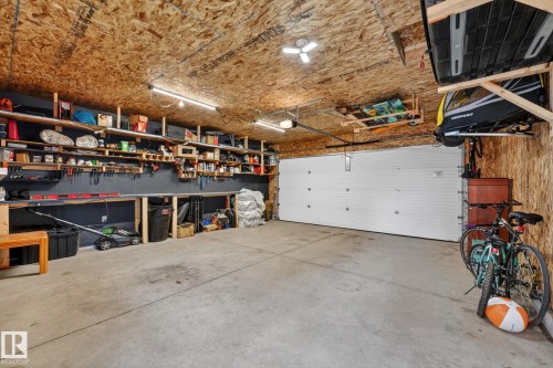 Spacious garage featuring a concrete floor, built-in shelving, two overhead storage racks, linear LED lighting, and a paneled garage door - 165 Robinson Drive, Leduc, AB 