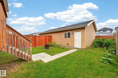 Expansive backyard featuring a detached outbuilding with tan siding and a white door, a wood deck with stairs, and a red wood privacy fence - 165 Robinson Drive, Leduc, AB 