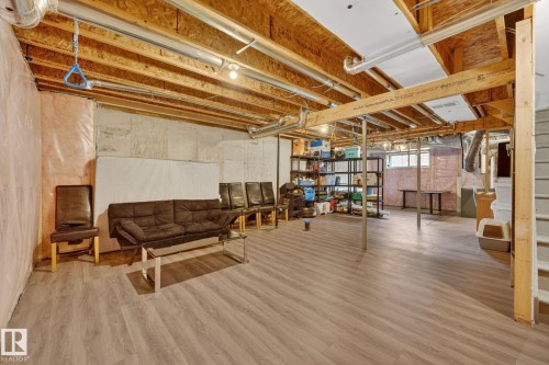 Spacious unfinished basement with wood-finish flooring, exposed ceiling joists, concrete foundation walls, and visible utility infrastructure - 165 Robinson Drive, Leduc, AB 