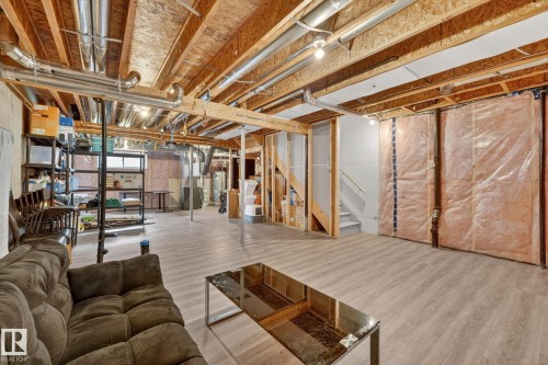 Expansive unfinished basement featuring wood-finish flooring, exposed ceiling joists, and visible insulation for future customization - 165 Robinson Drive, Leduc, AB 