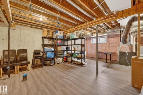 Unfinished basement featuring exposed wood joists, concrete walls, and wood-finish flooring - 165 Robinson Drive, Leduc, AB 