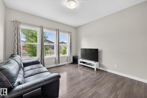 Bright living space featuring three large windows, wood-finish flooring, light grey painted walls, and white baseboards - 165 Robinson Drive, Leduc, AB 