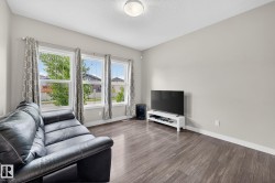 Bright living space featuring three large windows, wood-finish flooring, light grey painted walls, and white baseboards - 