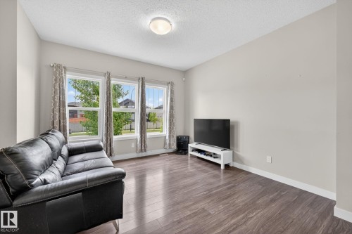 Living area with three large windows, wood-finish flooring, a neutral wall color, white baseboards, and a flush-mount ceiling light fixture - 165 Robinson Drive, Leduc, AB 