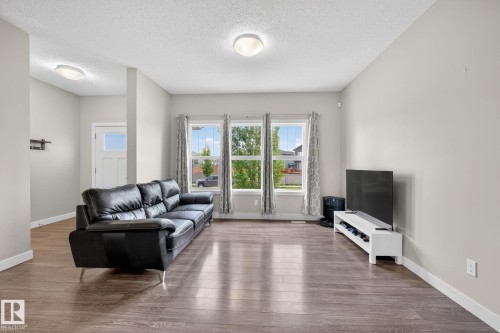 Spacious living area featuring wood-finish flooring, light grey walls, and a trio of windows - 165 Robinson Drive, Leduc, AB 