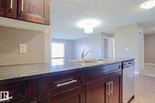 Kitchen featuring dark wood cabinetry, granite-finish countertops, and a stainless steel double basin sink - 405 11804 22 Avenue Sw, Edmonton, AB 