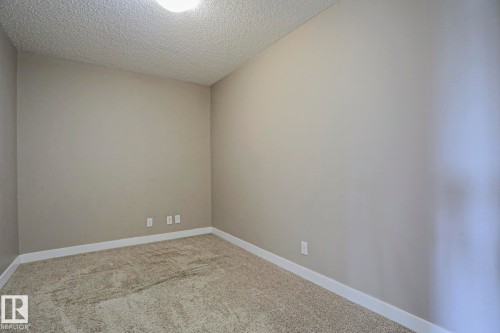 Neutral-toned room featuring light gray walls, textured carpeting, and white baseboards - 405 11804 22 Avenue Sw, Edmonton, AB 