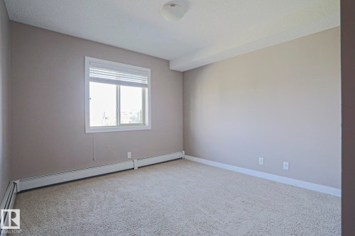 Carpeted room with neutral tone painted walls, white baseboards, and a window with blinds - 405 11804 22 Avenue Sw, Edmonton, AB 