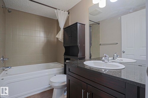 Bathroom featuring a dark wood-finish vanity with an integrated sink, a dark speckled countertop, and a wall-mounted mirror - 405 11804 22 Avenue Sw, Edmonton, AB 