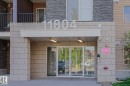 Building entrance featuring a stone block facade, glass double doors, an overhead awning with recessed lighting, and large building numbers - 405 11804 22 Avenue Sw, Edmonton, AB 