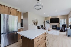 Kitchen island with white countertop and integrated storage, stainless steel French door refrigerator, wood-finish flooring, recessed lighting, and a fireplace with a mantel - 