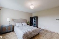 Neutral-toned bedroom featuring wood-finish flooring, a contemporary ceiling light fixture, and a light-colored accent wall - 
