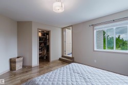 Spacious room featuring wood-finish flooring, a walk-in closet, a multi-pane window, neutral wall tones, and a flush-mount ceiling light - 