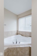 Corner soaking tub with chrome fixtures, surrounded by neutral-toned tile - 
