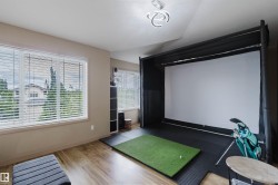 Dedicated recreation room featuring wood-finish flooring, multiple windows with blinds, a built-in golf simulator with a large projection screen, and a recessed ceiling light fixture - 