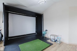 Dedicated indoor golf simulation area with a large projection screen, padded enclosure, and integrated putting green - 