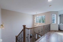 Upper landing featuring wood-finish flooring, a contemporary chandelier, and a decorative wrought iron and wood staircase railing - 