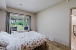 Room featuring wood-finish flooring, a large window offering outdoor scenery, and a doorway opening to a hallway with a wood staircase - 