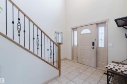 Entryway featuring light-toned ceramic tile flooring, a solid panel door with a half-round lite, decorative sidelites, and a staircase with wrought iron balusters and a wood handrail - 
