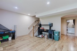 Spacious lower-level area with wood-finish flooring, recessed lighting, and a finished staircase with wood railing and metal spindles - 
