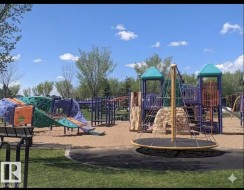 Community playground with multiple play structures, sand base, and surrounding green space - 