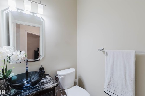 Bathroom featuring a vessel sink with a black glass bowl, a dark stone-finish countertop, and a chrome faucet - 20524 58 Avenue, Edmonton, AB 