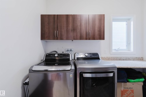 Dedicated laundry area featuring wood-finish overhead cabinetry, a light-toned speckled countertop, and a white framed window - 20524 58 Avenue, Edmonton, AB 