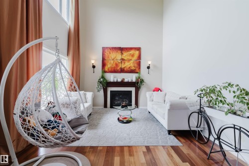 Living area featuring a two-story ceiling, wood-finish flooring, and a fireplace with a dark wood mantel - 20524 58 Avenue, Edmonton, AB 