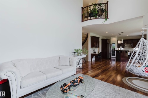 Two-story living area with high ceilings, warm wood-finish flooring, and a curved architectural balcony - 20524 58 Avenue, Edmonton, AB 