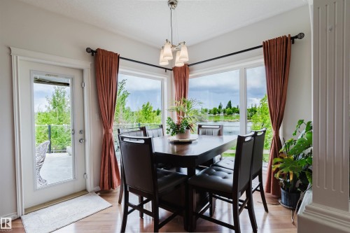 Dining area featuring wood-finish flooring, a contemporary chandelier, and large windows - 20524 58 Avenue, Edmonton, AB 