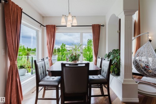 Dining area featuring wood-finish flooring, a contemporary chandelier, expansive windows, and a decorative architectural column - 20524 58 Avenue, Edmonton, AB 