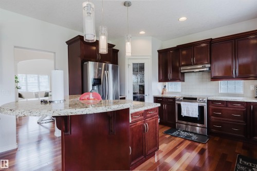 Kitchen featuring rich wood cabinetry, stainless steel appliances, speckled stone countertops, and wood-finish flooring - 20524 58 Avenue, Edmonton, AB 