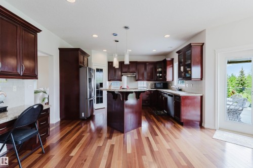 Open-concept kitchen featuring wood-finish flooring, dark wood cabinetry with crown molding, and a central island with pendant lighting - 20524 58 Avenue, Edmonton, AB 