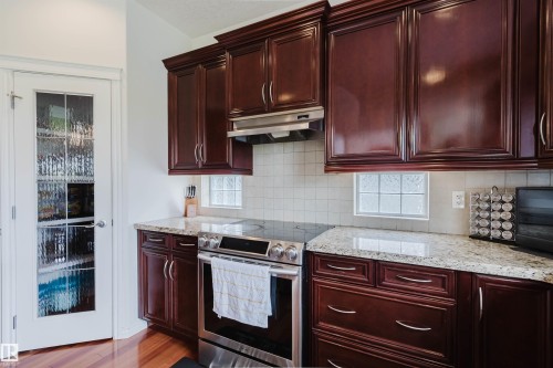 Kitchen featuring dark wood cabinetry, light granite countertops, a stainless steel electric range with a matching range hood, and a tiled backsplash - 20524 58 Avenue, Edmonton, AB 